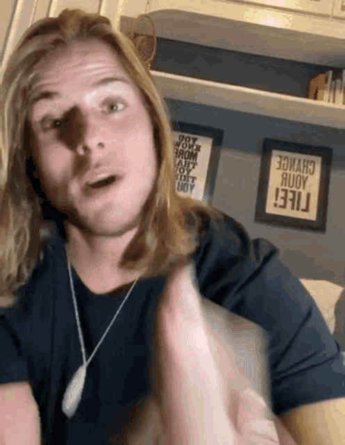 a man with long blonde hair is standing in front of a wall that has a sign that says " i feel "