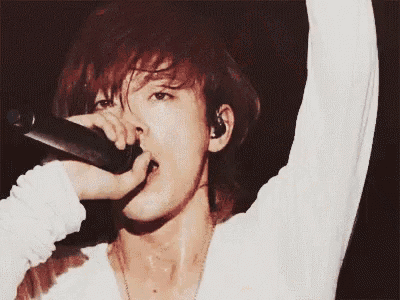 a man with red hair is singing into a microphone while wearing a white shirt