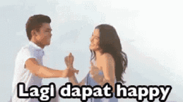 a man and a woman are dancing on a beach with the words lagi dapat happy written above them .