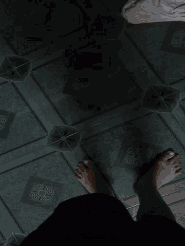 a person 's feet are standing on a tiled floor with a pattern of squares with the letter g on them