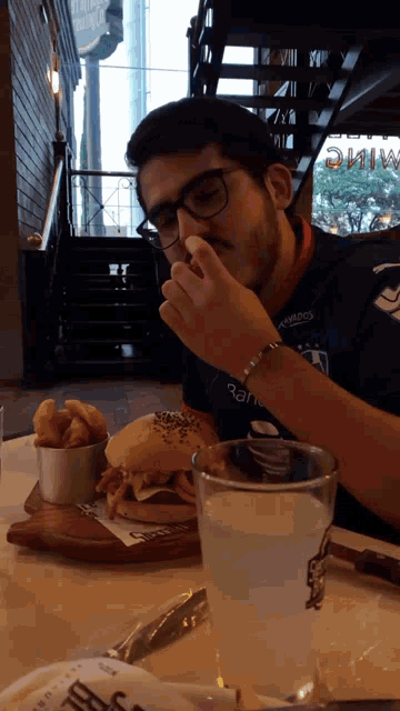 a man wearing a blue shirt that says ' atletico ' on it is eating a hamburger