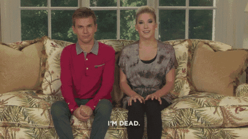 a man and a woman are sitting on a couch and the woman is saying i 'm dead