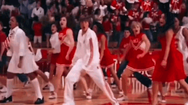 a man and a group of cheerleaders are dancing on a basketball court .