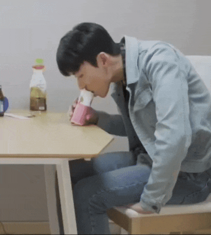 a man is sitting at a table drinking from a pink cup