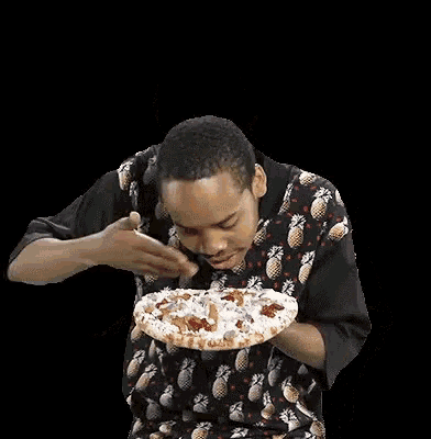 a man in a pineapple shirt is holding a pizza in his hand .