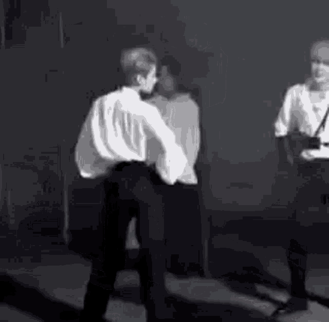 a black and white photo of a group of people dancing on a stage in a dark room .