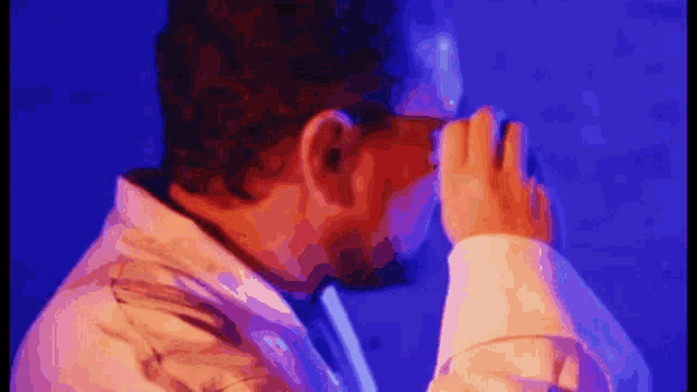a man covering his face with his hand in front of a blue wall
