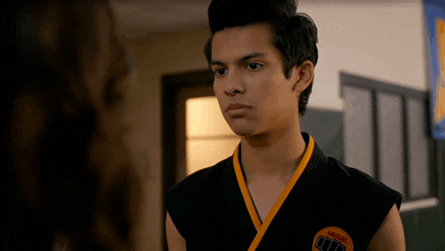 a young man in a black and yellow karate uniform looks at a girl
