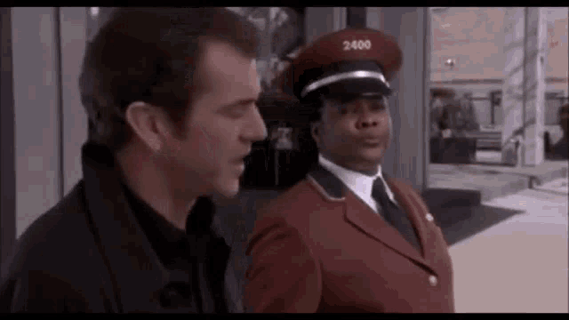 a man in a black jacket is talking to a security guard in a red uniform .