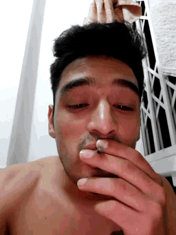 a shirtless man is smoking a cigarette with a towel on his head