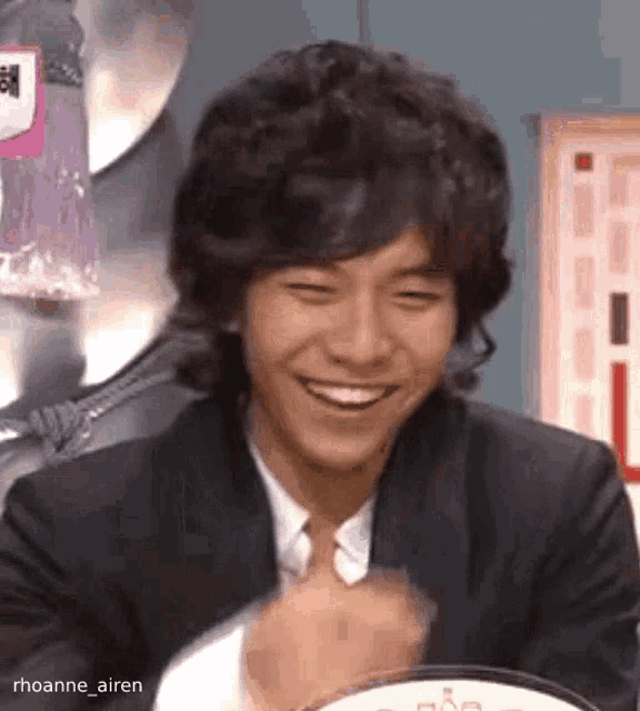 a young man in a suit and tie is smiling and laughing while sitting at a table .