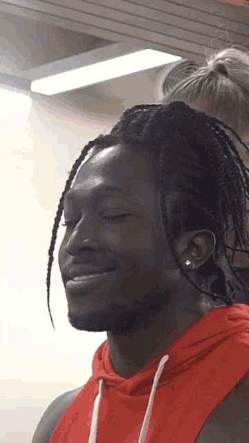 a man with braids is wearing a red hoodie and earrings