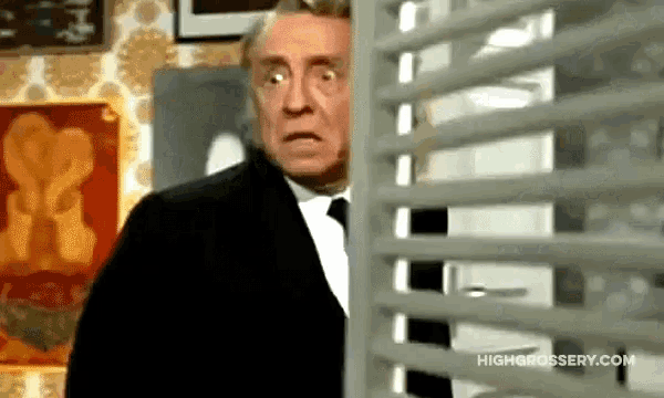a man in a suit and tie is peeking through a window blind .