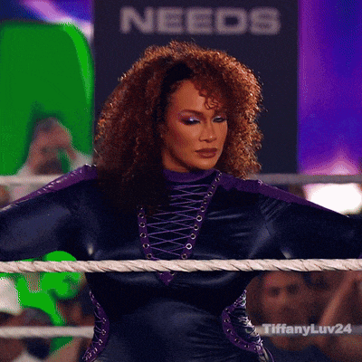 a woman in a black and purple outfit stands in a ring with a sign that says needs in the background