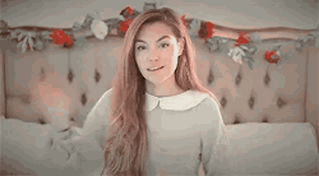 a woman with long red hair is sitting on a bed with flowers on the headboard .