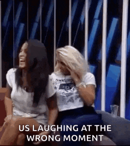 two women are laughing at the wrong moment while sitting on a couch .