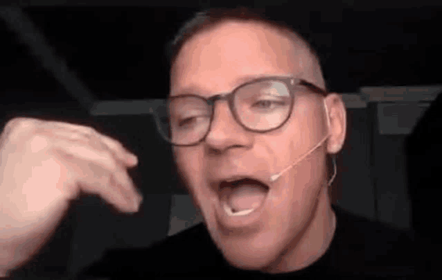 a man wearing glasses and a microphone is talking .