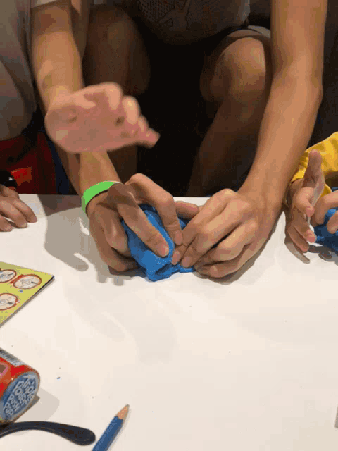 a person with a green wristband is playing with blue clay on a table
