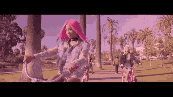 a woman with pink hair is riding a bicycle in a park