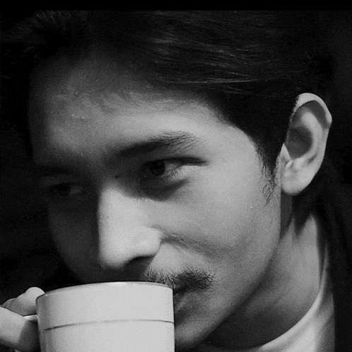 a man with a mustache is drinking from a white mug