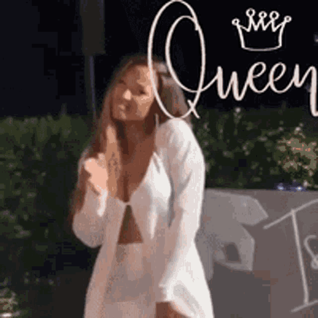 a woman in a white dress is standing in front of a sign that says queen
