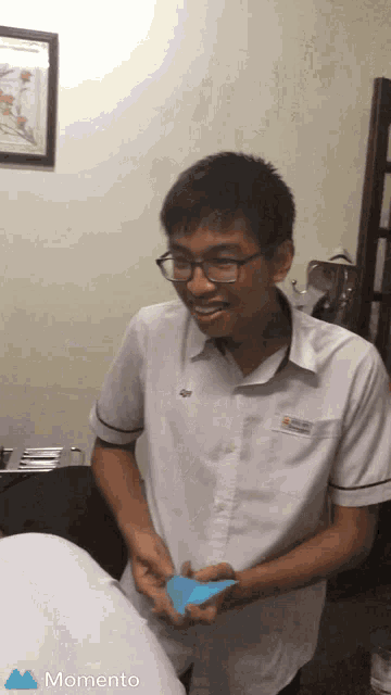 a man in a white shirt is smiling and holding a piece of paper with the word momento on the bottom right