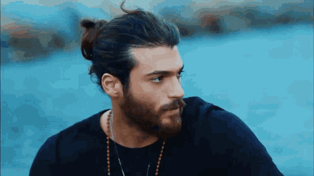 a man with long hair and a beard is wearing a black shirt and necklace