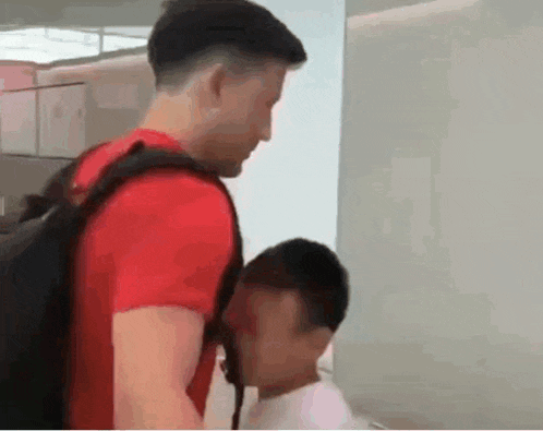 a man in a red shirt is standing next to another man with a backpack .