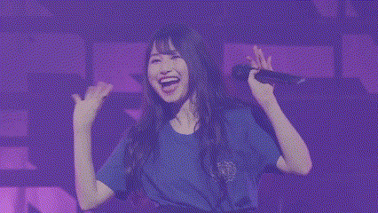 a woman in a blue shirt is holding a microphone in her hand and smiling .