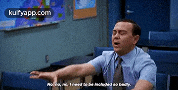 a man in a suit and tie is sitting in a classroom with his arms outstretched .