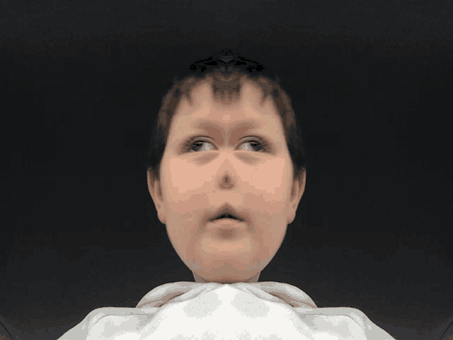 a close up of a child 's face with a white shirt around his neck