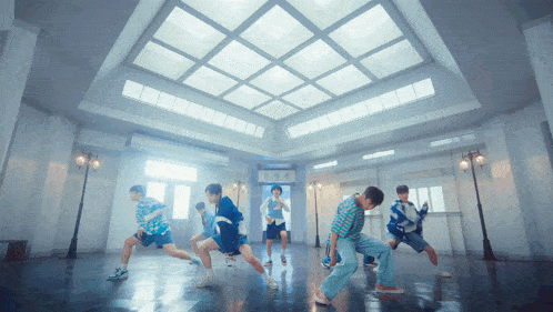 a group of young men are dancing in a large room with a ceiling that has squares on it