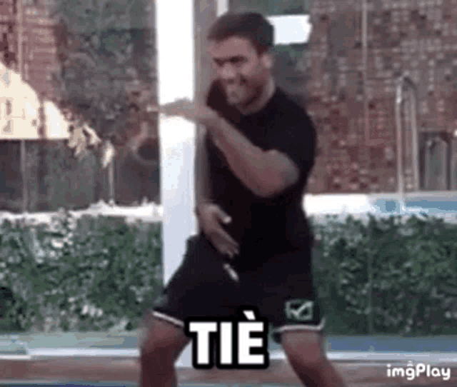 a man in a black shirt and black shorts is dancing in front of a window with the word tie on it .