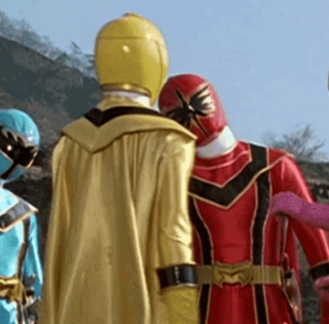 a group of power rangers are standing next to each other and one is wearing a yellow cape .