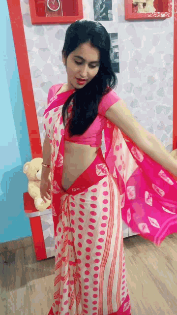 a woman in a pink and white polka dot saree is standing in front of a teddy bear