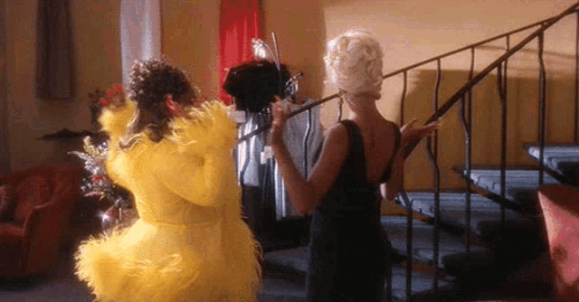 a woman in a yellow feathered dress stands next to another woman in a black dress