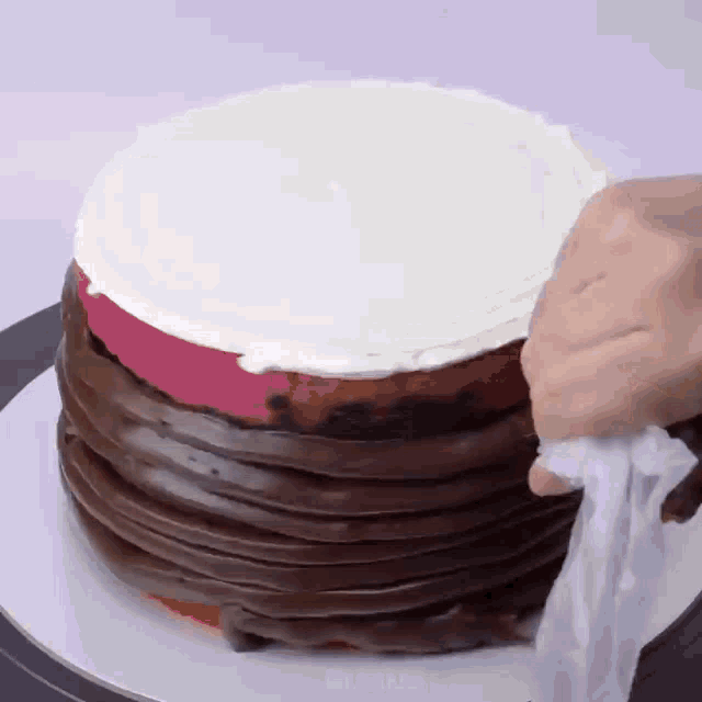 a person is frosting a chocolate cake with white frosting ..