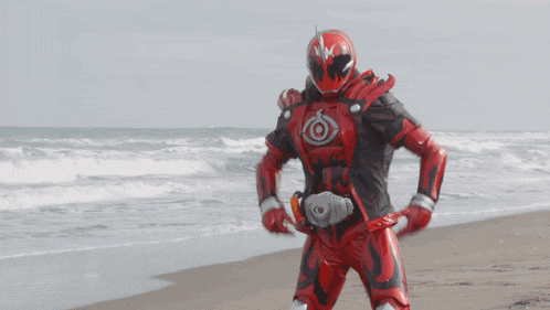 a man in a red superhero costume is holding a red sword on the beach