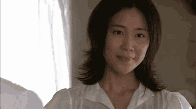 a woman wearing a white shirt and a necklace looks at the camera