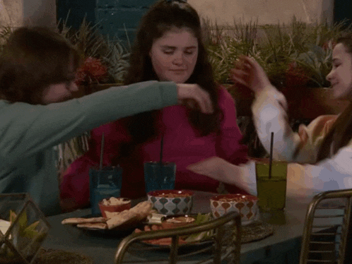 a group of girls are sitting at a table with plates of food and drinks