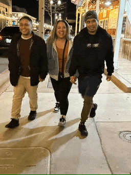 three people are walking down a sidewalk and one of them is wearing a hoodie that says e.m.