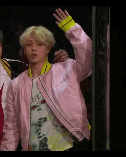 a man wearing a pink jacket and a gucci shirt waves