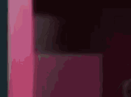 a blurry picture of a woman in a black dress standing in front of a pink wall .