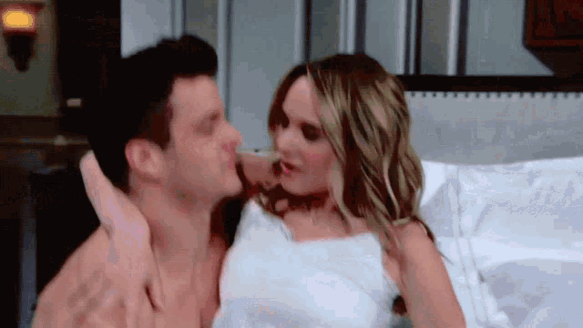 a man and a woman are kissing on a bed covered in white sheets
