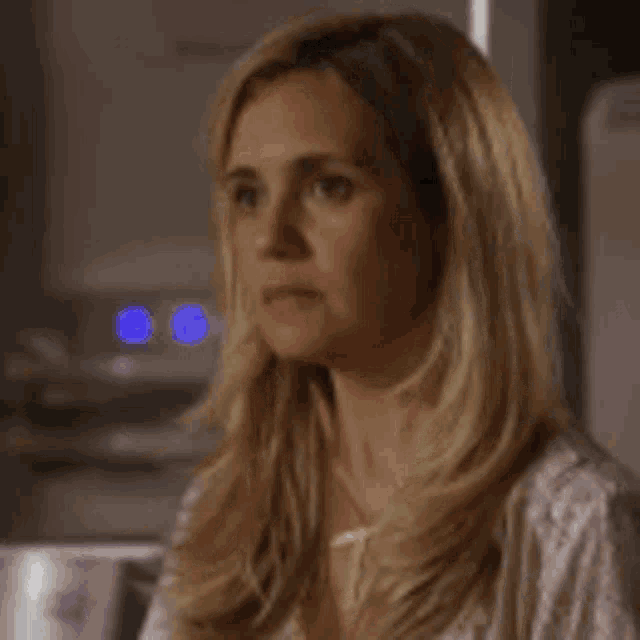a woman with long blonde hair is wearing a necklace and earrings and making a funny face .