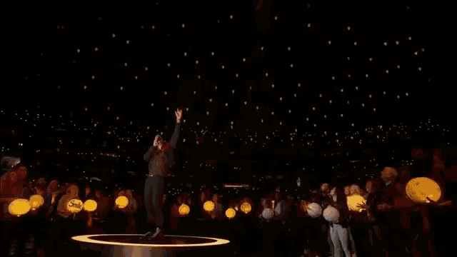 a man is singing into a microphone on a stage in front of a crowd of people holding lanterns .