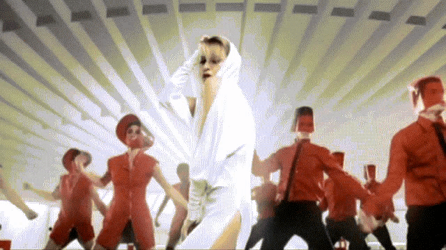 a woman in a white robe is surrounded by a group of men in red uniforms