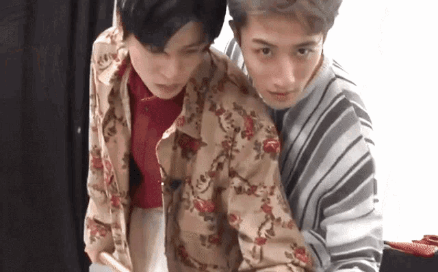 two young men are standing next to each other and one of them is wearing a floral jacket .
