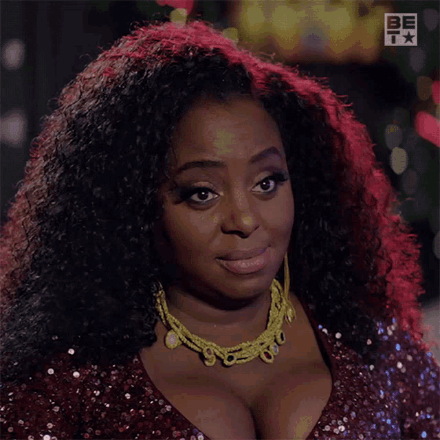 a woman wearing a red sequined dress and a gold necklace with the letters be on the bottom