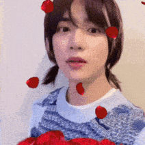 a woman in a blue sweater is holding a bouquet of red roses in front of her face .